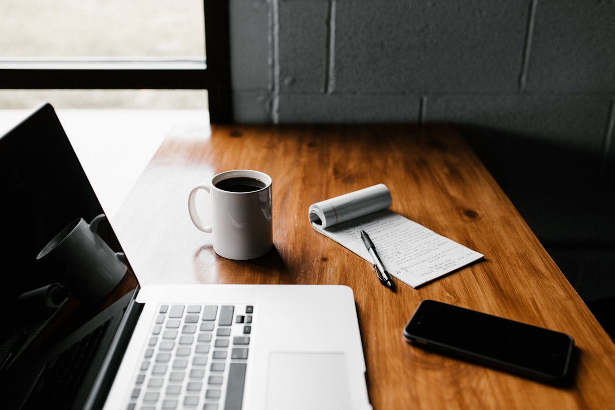 Portátil, cuaderno y una taza de café sobre una mesa de madera